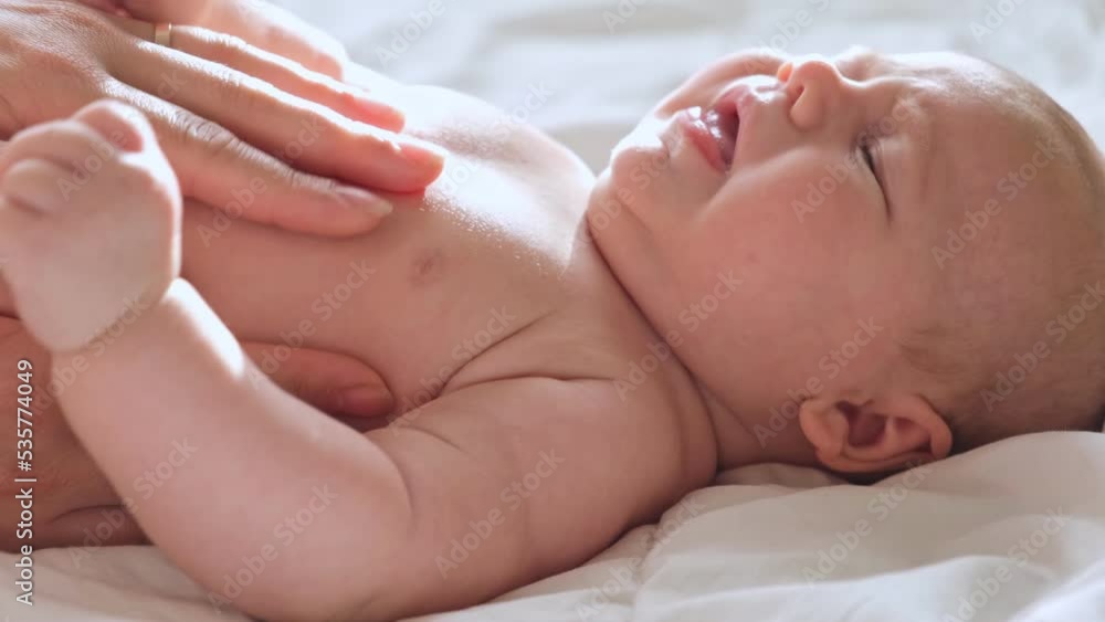 Mother doing Massage to Baby at Home, Playing with Child. Light Background. Infant Baby Massage. Mom makes Massage for Newborn, Apply Oil. Early Age Children Development. Authentic Candid Lifestyle Mother doing Massage to Baby at Home, Playing with Child. Light Background. Infant Baby Massage. Mom makes Massage for Newborn, Apply Oil. Early Age Children Development. Authentic Candid Lifestyle