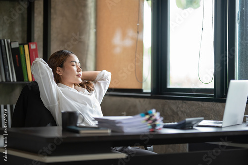 Taking time for a break. businesswoman holding hands behind her head and keeping her eyes closed while sitting at her working place.