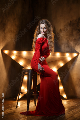 Beauty fashion portrait of elegant woman in red against the backdrop of a glowing star.
