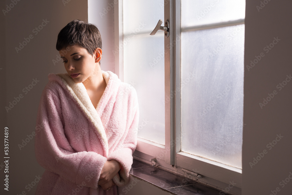 Young woman cancer patient standing in front of hospital window Young woman cancer patient standing in front of hospital window