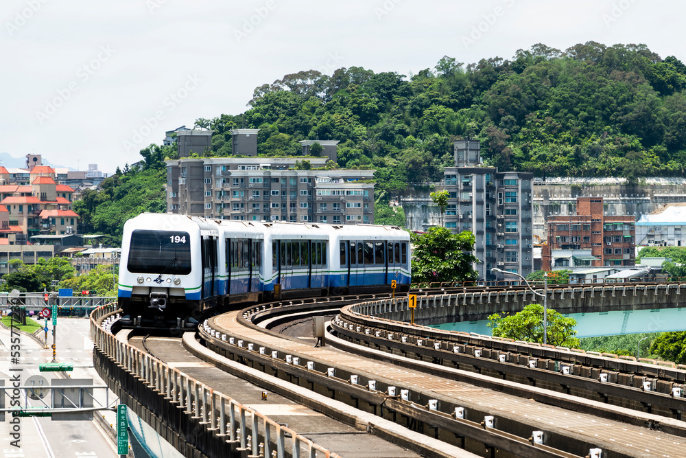 Naklejka premium Wenhu or Brown line of Taipei MRT in Taiwan. the train running on elevated rails of the Taipei Metro System between buildings under the clear blue sky.