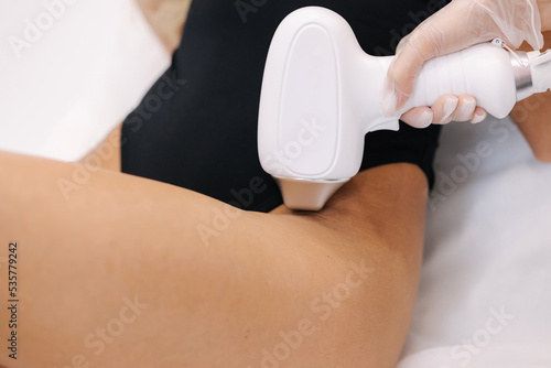 Cosmetology. Beautiful woman receiving laser hair removal procedure at beauty salon. Beautician doing beauty treatment for female arm at spa salon. Protective glasses. Close-up of bikini area