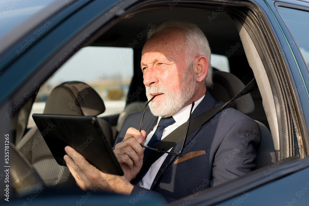 Senior businessman using tablet for traffic navigation while sitting in the car on the parking lot Senior businessman using tablet for traffic navigation while sitting in the car on the parking lot