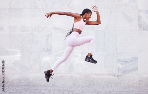 Fototapeta Naklejka Na Ścianę i Meble -  Energy, sports and black woman jump running outdoor for fitness, wellness and outdoor training with wall mockup. Young, healthy african girl in athlete runner clothes for fashion mock up background