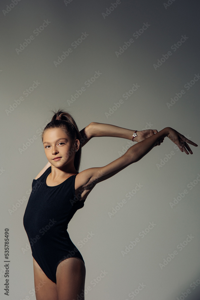 Gymnast child girl trains against gray background.
