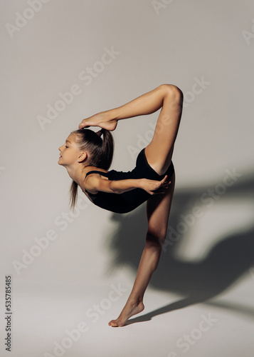 Gymnast child girl exercises against gray background.