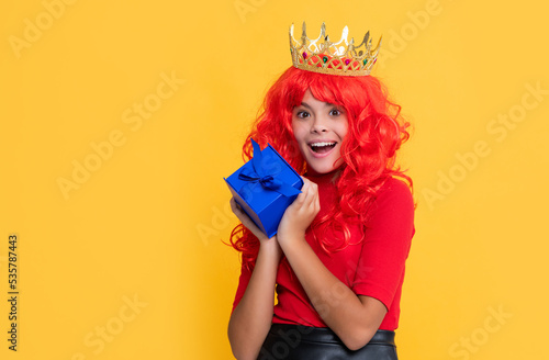 surprised girl in crown with present box on yellow background © be free