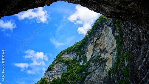 landscape with sky,  The high cliffs that surround the beach in Nusa Penida from under the cliff are like coming out of a cave with a blue sky roof photo