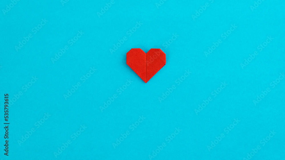 Red origami heart on blue background