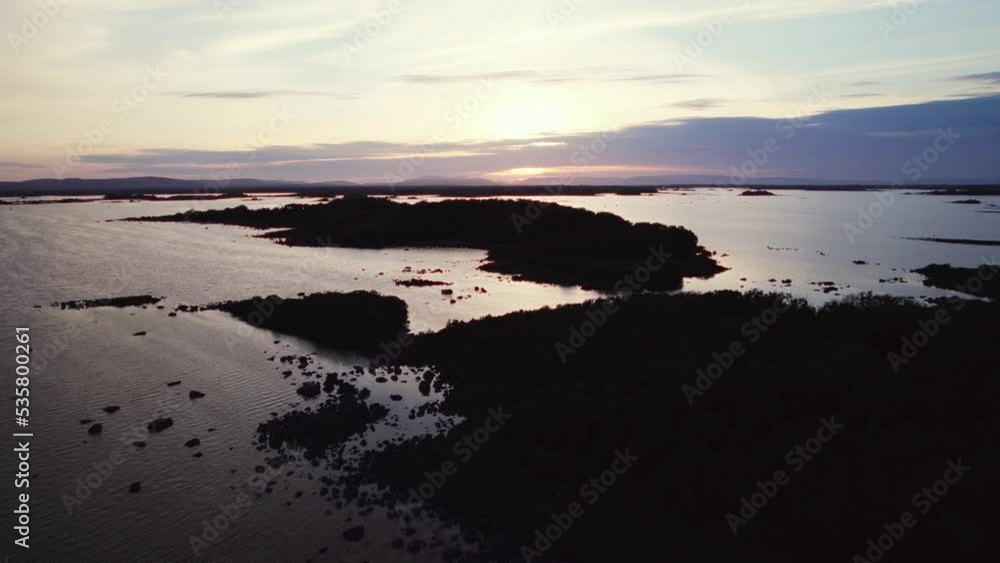 Beautiful aerial flying over gigantic irish lough Corrib with many small island silhouettes in the water beneath. View into the distance. Flying backward during blue hour golden evening sun reflecting Beautiful aerial flying over gigantic irish lough Corrib with many small island silhouettes in the water beneath. View into the distance. Flying backward during blue hour golden evening sun reflecting