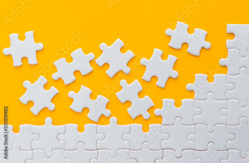 Unfinished white puzzle pieces on yellow background