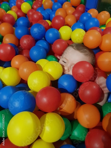 white baby boy playing with colourful balls ball pool 