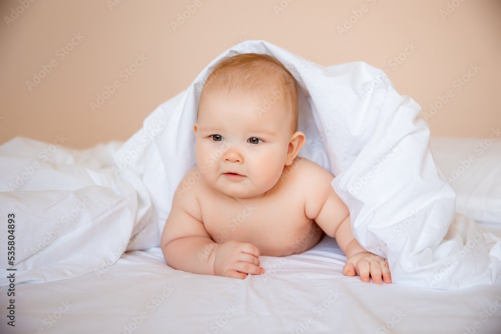 baby boy in a diaper is lying on a white sheet, covered with a blanket in the bedroom on the bed baby boy in a diaper is lying on a white sheet, covered with a blanket in the bedroom on the bed