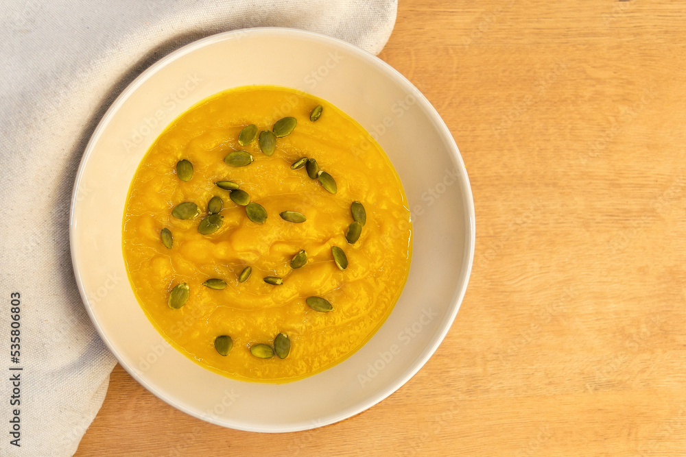 Pumpkin puree soup in a white plate with pumpkin seeds and croutons close-up. Vegetable autumn dish for Halloween or Thanksgiving. Pumpkin puree soup in a white plate with pumpkin seeds and croutons close-up. Vegetable autumn dish for Halloween or Thanksgiving.