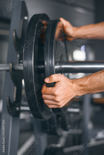 Strong male hands add weight plates to the barbell in the gym