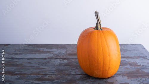 A beautiful large orange pumpkin lies on an old dark wooden table with shabby paint, against a white wall. Copy space view. Autumn harvest, symbol of autumn. Selective focus