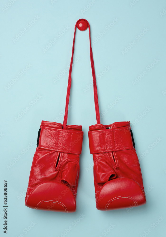 Red leather boxing gloves hanging on a cord, blue background.