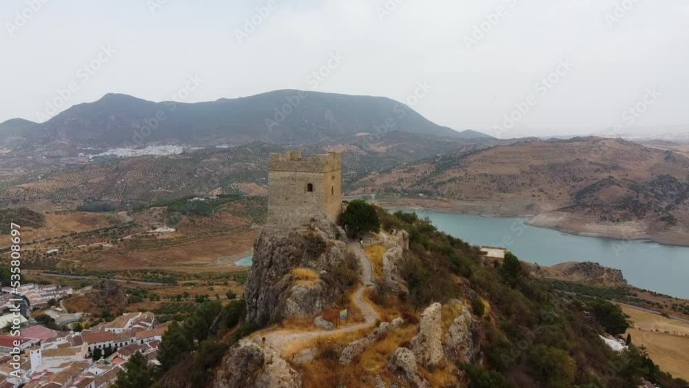 aerial approach and fly by medieval castle and its watchtower on top of a mountain. White traditional houses village blue lake and mountains aerial approach and fly by medieval castle and its watchtower on top of a mountain. White traditional houses village blue lake and mountains