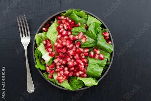 Healthy food pomegranate vegetable salad in bowl on black wood background.