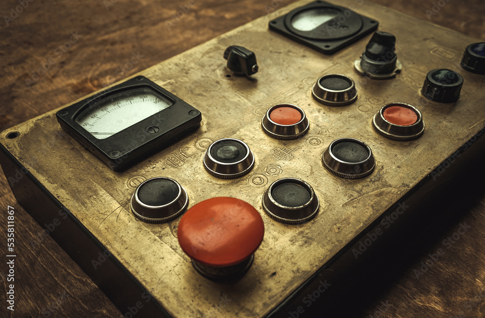 A large metal control panel with buttons and sensors on a wooden table. Red button on the control panel. A large metal control panel with buttons and sensors on a wooden table. Red button on the control panel.