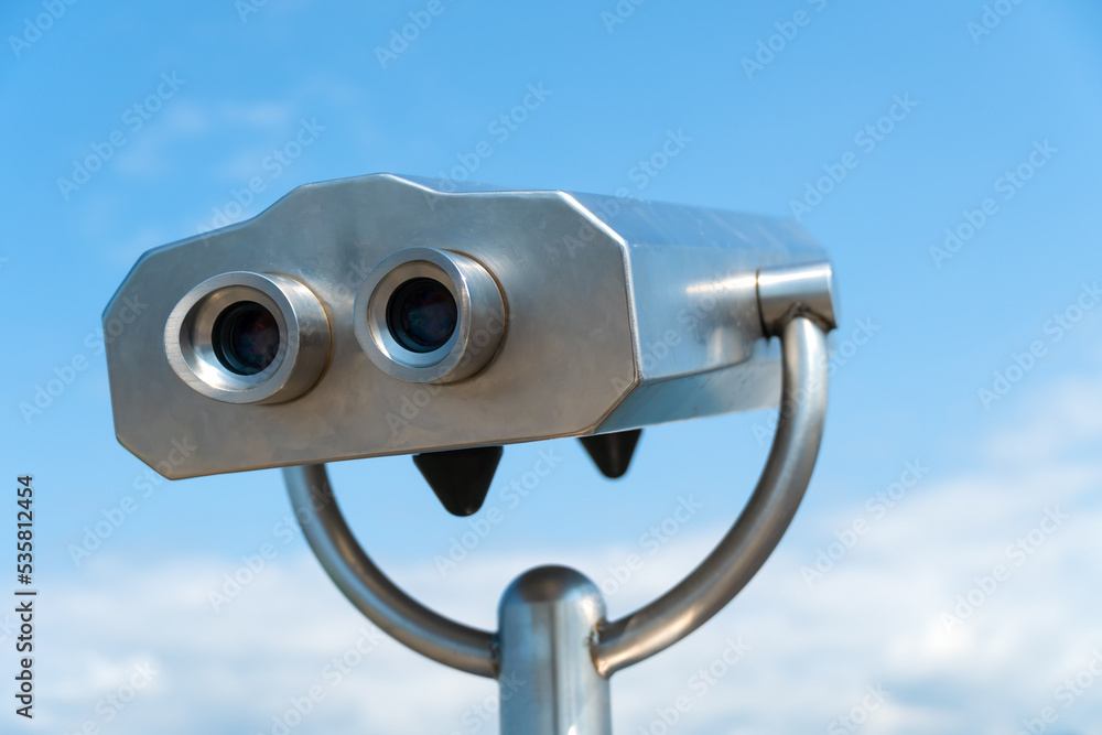 Close-up of a metal gray stationary binoculars on the observation deck against the blue sky on a sunny day. Bizarre imaginary metal man