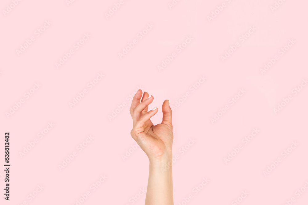 Mano de mujer en posición para sostener algo sobre un fondo rosa liso y aislado. Vista de frente y de cerca Copy space - obrazy, fototapety, plakaty 