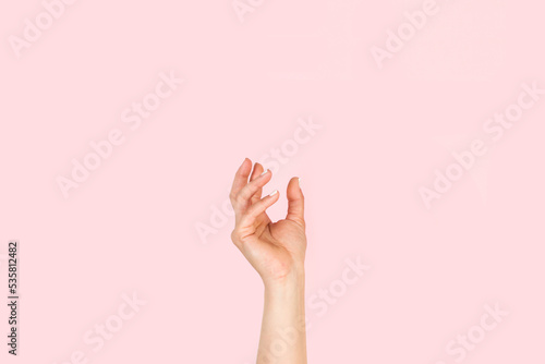 Mano de mujer en posición para sostener algo sobre un fondo rosa liso y aislado. Vista de frente y de cerca Copy space photo