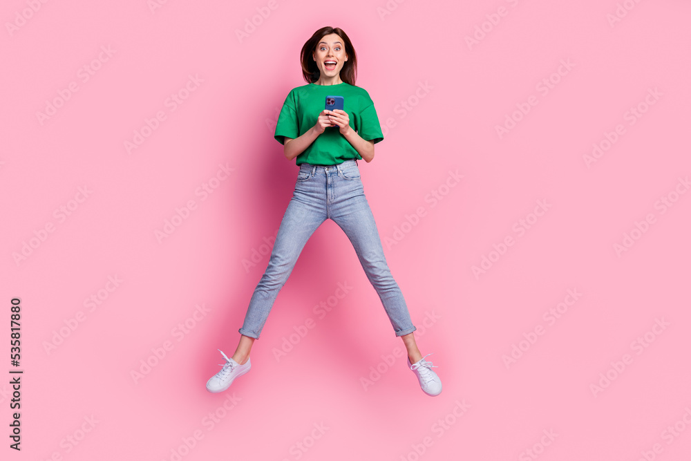 Full body photo of overjoyed carefree lady jumping hold use telephone isolated on pink color background Full body photo of overjoyed carefree lady jumping hold use telephone isolated on pink color background