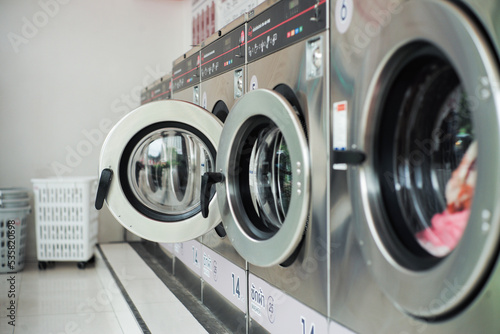 Selective focus on the front door of the washing machine with blurred close doors in foreground. Row of washers in the washing shop