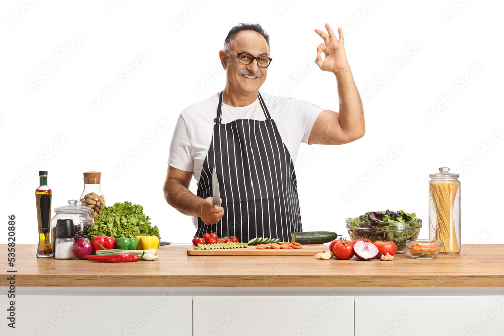 Portrait of a happy mature man gesturing ok sign behind a kitchen counter with vegetables Portrait of a happy mature man gesturing ok sign behind a kitchen counter with vegetables