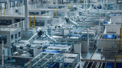 Large Production Line with White Industrial Robot Arms at Modern Bright Factory. Solar Panels are being Assembled on Conveyor. Automated Manufacturing Facility.