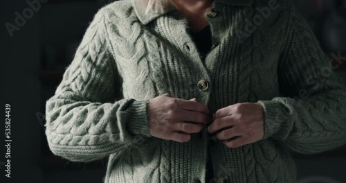 Woman Putting On Extra Jumper Clothing Trying To Keep Warm During Cost Of Living Energy Crisis