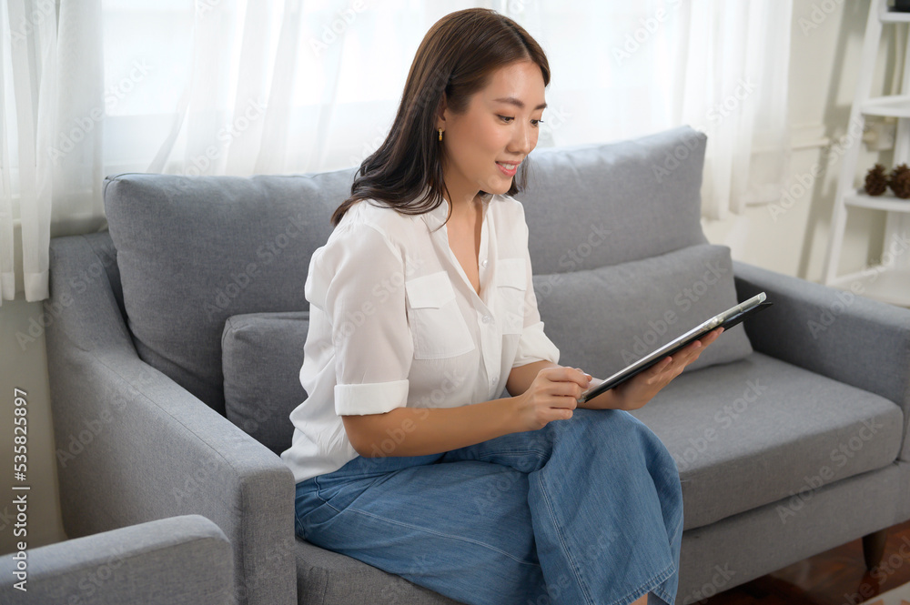 Young asian woman using tablet on sofa in living room. Young asian woman using tablet on sofa in living room.