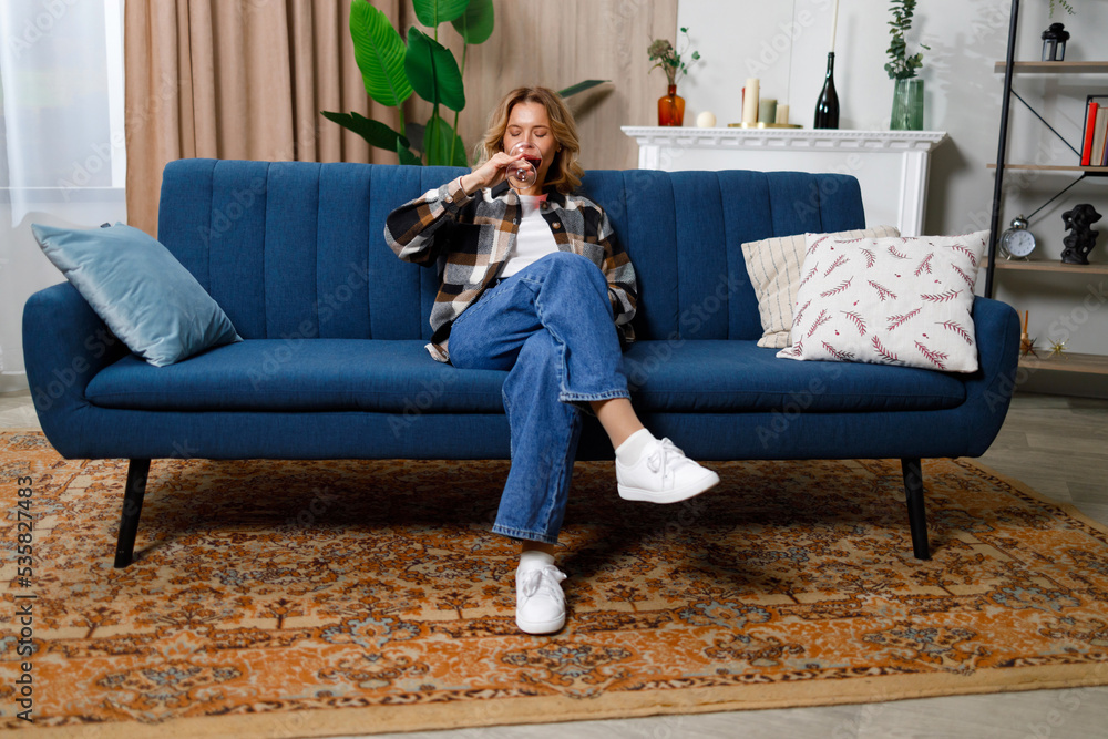 Obraz premium Mature woman drinking red wine sitting on sofa