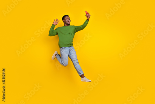 Full length body size view of handsome trendy cheery guy jumping taking selfie blog isolated on vivid yellow color background