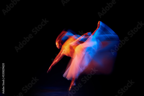 Futurism, fantasy, miracle. Graceful and fragile ballerina in ballet dress in motion isolated over black background in mixed neon light.