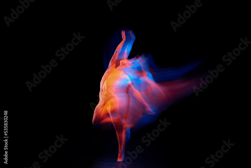 Like a phoenix. Solo performance of flexible adorable male ballet dancer isolated on dark background in glowing colorful neon light. Grace, art, beauty