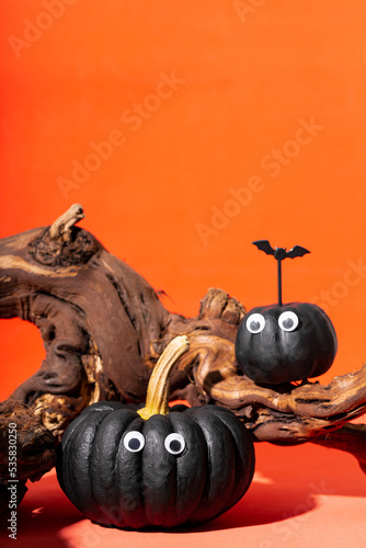Two black pumpkins with eyes and web spiders on an orange background. Pumpkin monsters, funny Halloween vertical card with copy space for text