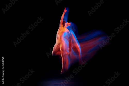 Young graceful and flexible shirtless male ballet dancer dancing isolated on dark background in glowing colorful neon light. Grace, art, beauty