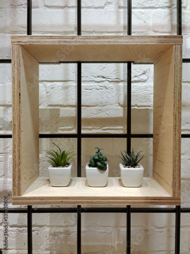 A decorative wooden square shelf with three flower pots hangs on a brick wall