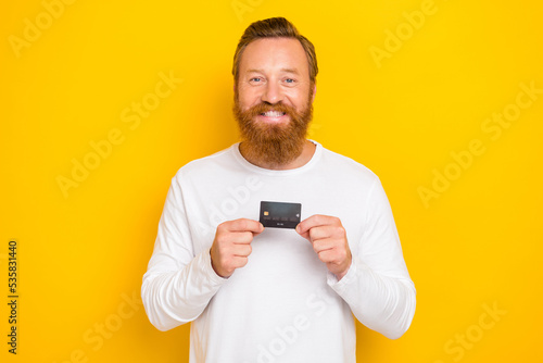 Photo of cheerful positive satisfied man wear stylish trendy clothes pullover recommend use bank card isolated on yellow color background