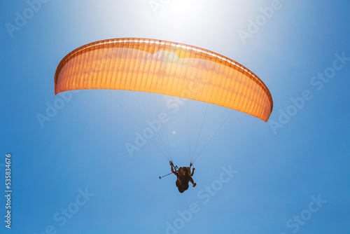 Tandem orange paragliding against a blue sky, sunny day.