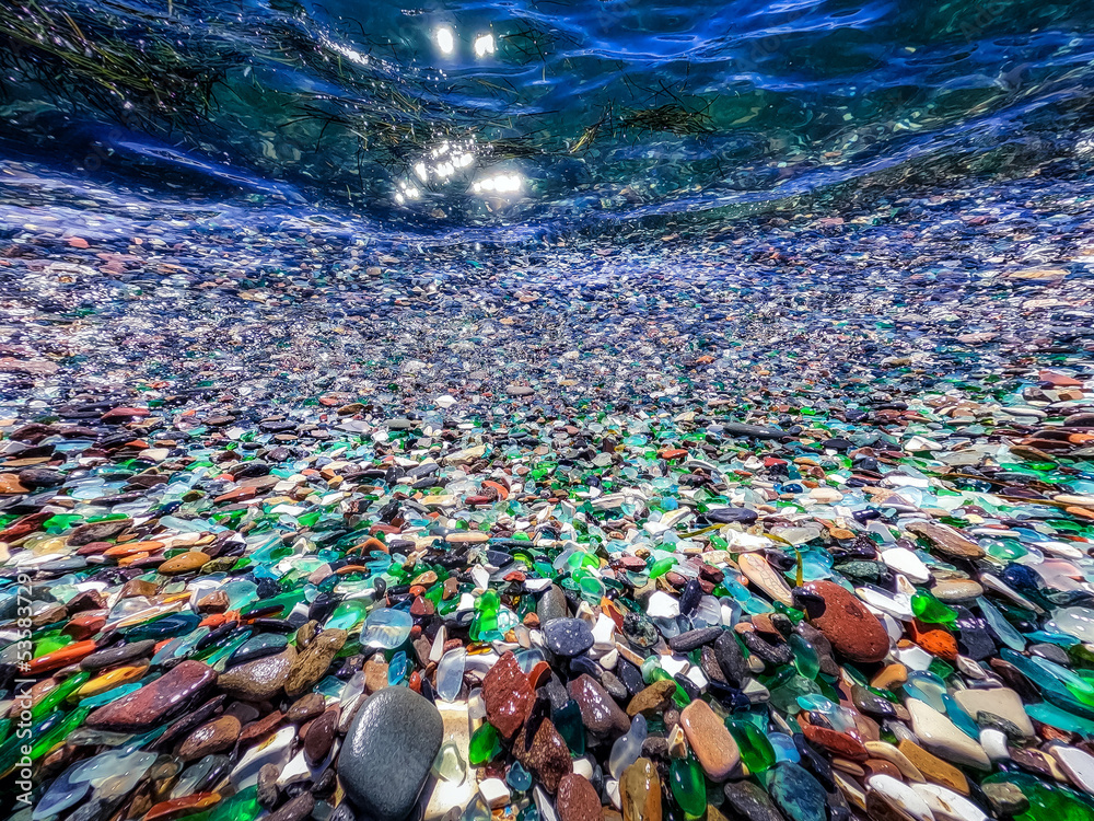 Beautiful underwater photo with natural polish textured sea glass and stones. Green, blue shiny glass with multi-colored sea pebbles close-up, emerald clear sea. High quality photo