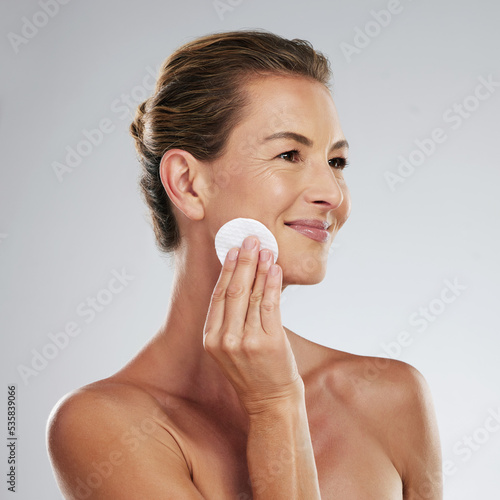 Mature woman, skincare and facial cotton on a gray studio background. Health, wellness and female model cleaning face and remove makeup, cosmetics or exfoliation for skin anti aging beauty treatment.