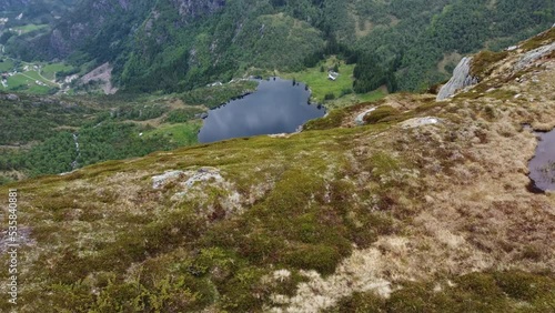 Countryside farmhouse and lake Leirovatnet seen from mountain peak viewpoint - Aerial moving sideways along cliff creating massive parallax effect - Eidslandet in Vaksdal Norway photo