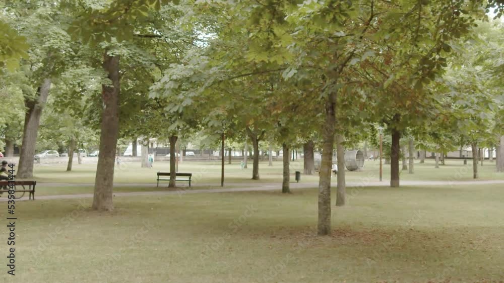 Side tracking shot of a park with cyclist and kids playing in the distance in slow motion 60fps Side tracking shot of a park with cyclist and kids playing in the distance in slow motion 60fps