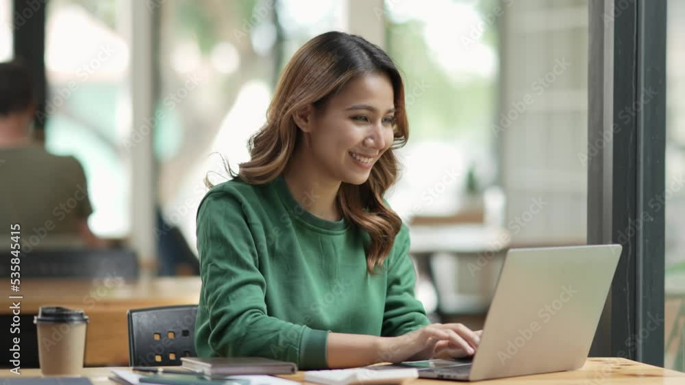 Cute young Asian woman sitting at cafe with her laptop happily. Asia female working on laptop computer at home. Cute young Asian woman sitting at cafe with her laptop happily. Asia female working on laptop computer at home.