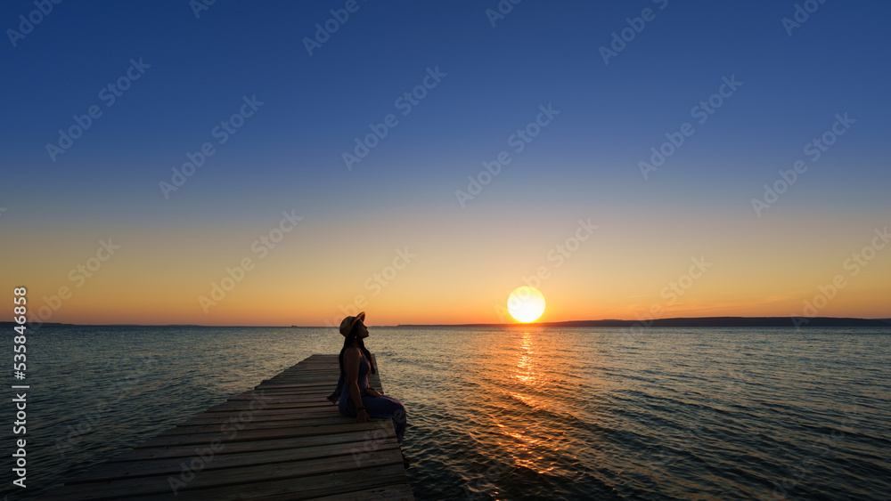 Traveler asian woman with her summer vacations on a twilight by the sea her sitting on bridge lonely dramatic lifestyle. Aegean Sea Beach, Canakkale, Turkye. Leave a blank and space for text entry.