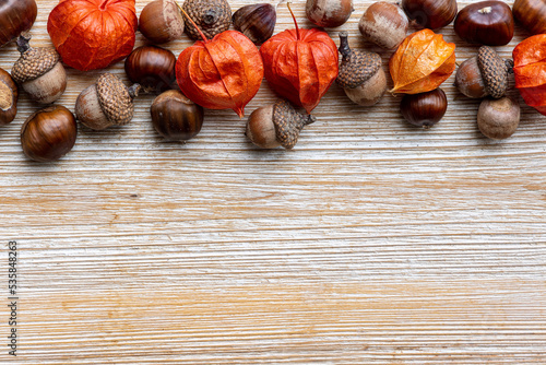 Autumn top border on wooden background. Above vieuw with chestnuts, acorns, and orange physalis laterns. Copy space. photo