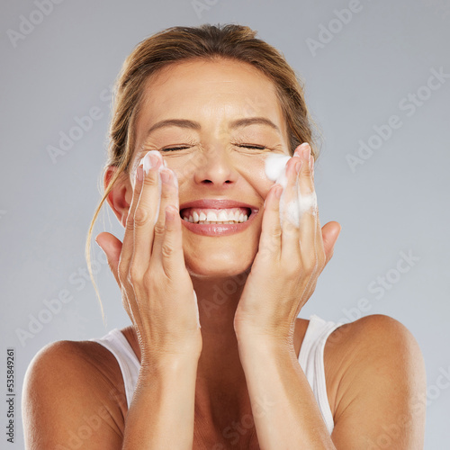 Foto Face, cleaning and hygiene with a mature woman washing her skin in studio on a gray background